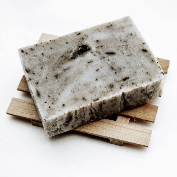 Cream soap bar with gray swirls sitting on a wooden soap holder with a white background.