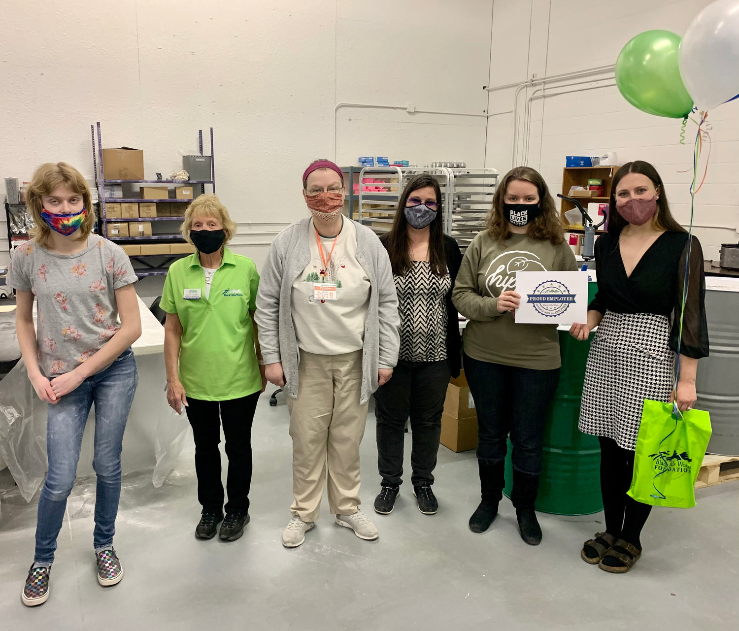 6 women in a warehouse with masks on holding an award.