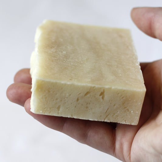 Cream colored soap bar being held in hand with a white background.
