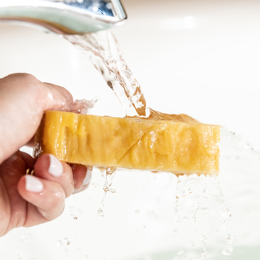 Orange soap bar with water from a faucet running over it being held in hand.