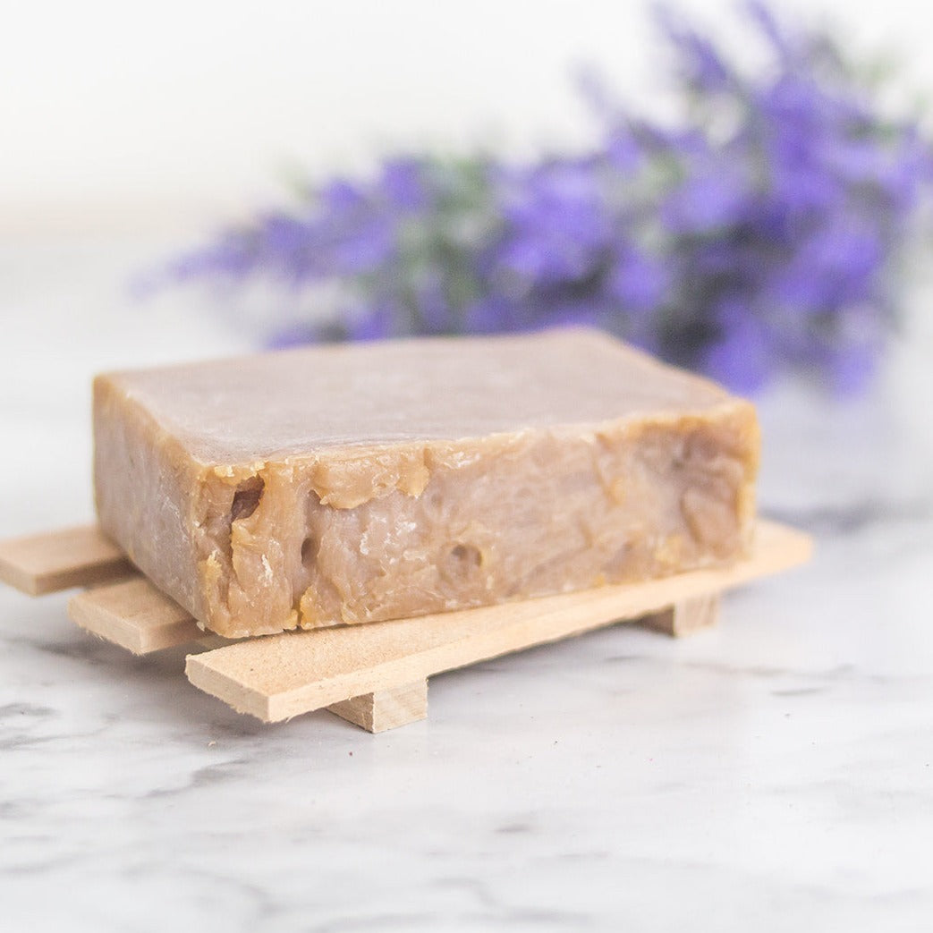 Purple soap bar on a wooden soap holder with a bunch of lavender in the background.
