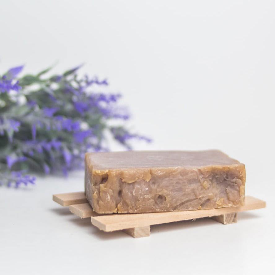 Purple soap bar on a wooden soap holder with a bunch of lavender in the background.