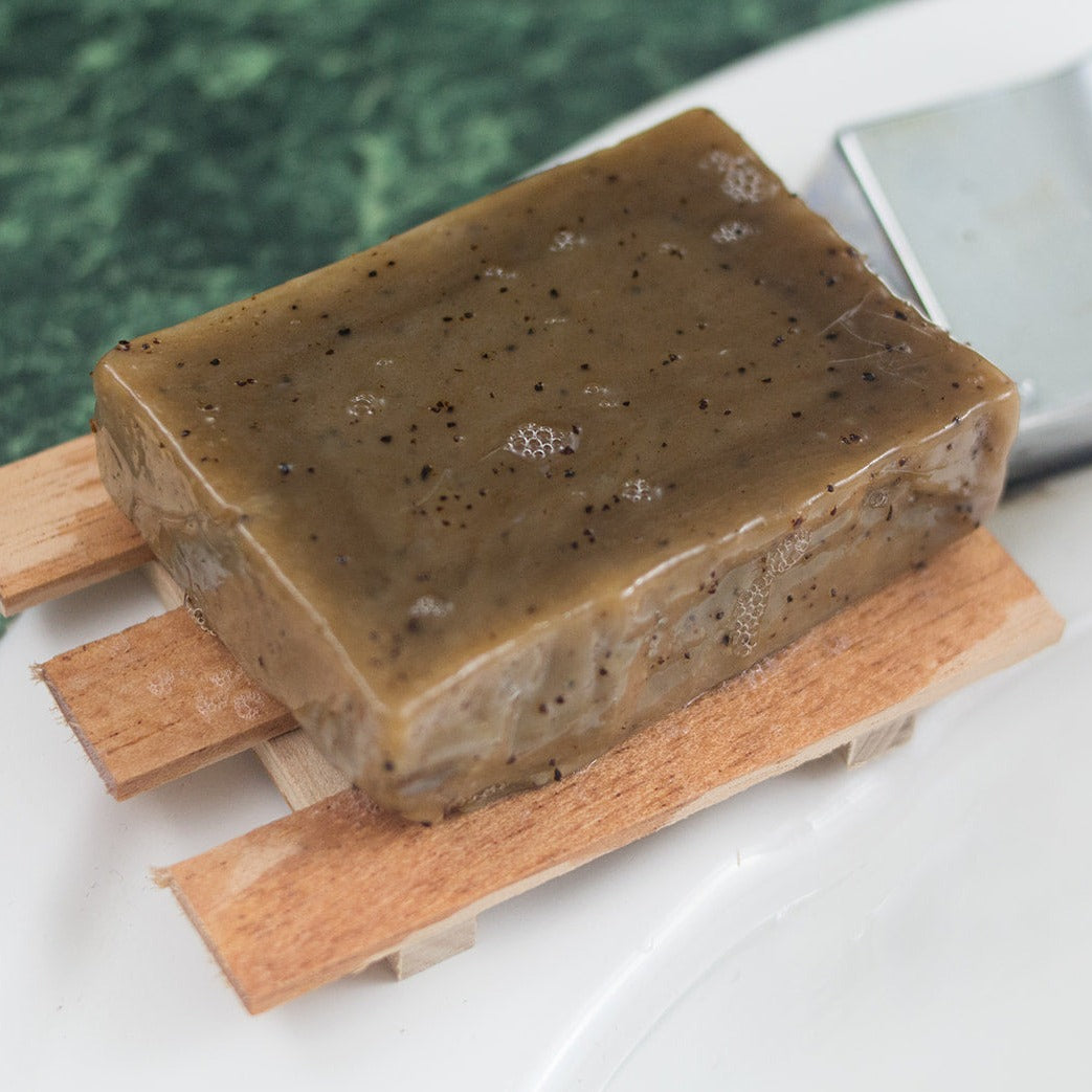 Sudsy brown soap bar with black coffee specks sitting on a wooden soap holder.