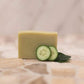 Light green soap bar on a white background decorated with cucumber slices and spearmint leaves.