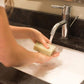 A woman lathering her hands at a sink with a light green soap bar.