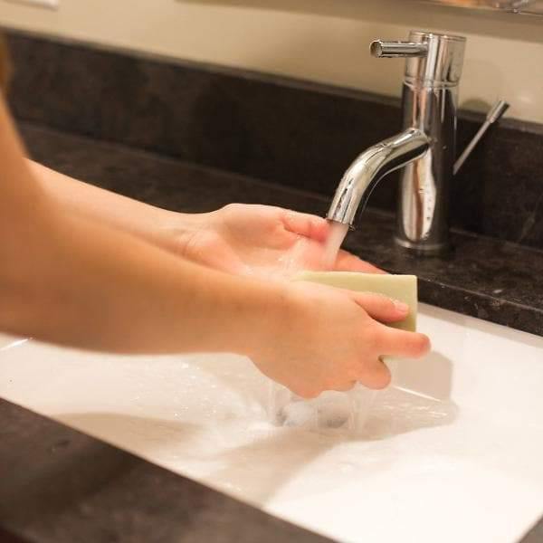 A woman lathering her hands at a sink with a light green soap bar.
