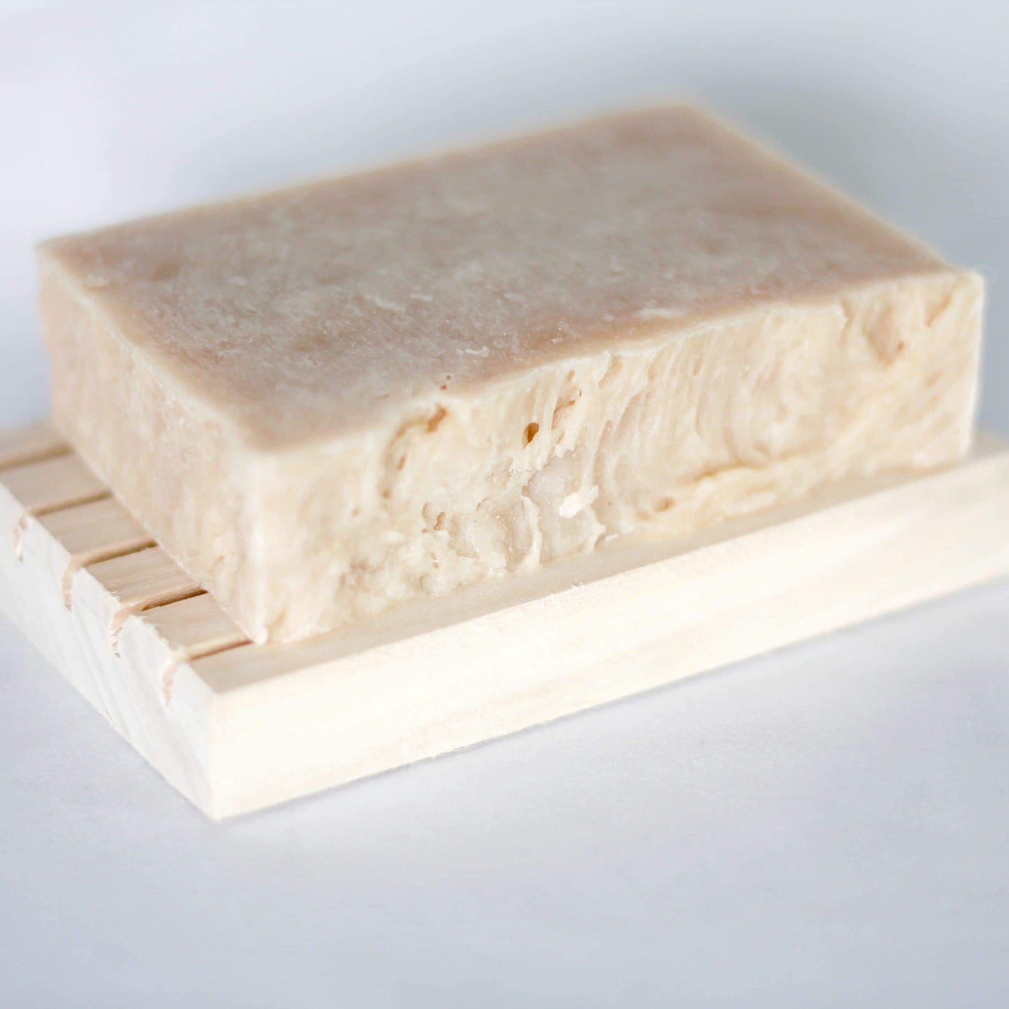 Cream soap bar on top of a wooden soap holder with a white background.