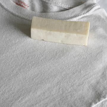 A cream colored stick of stain remover sitting on a white shirt.