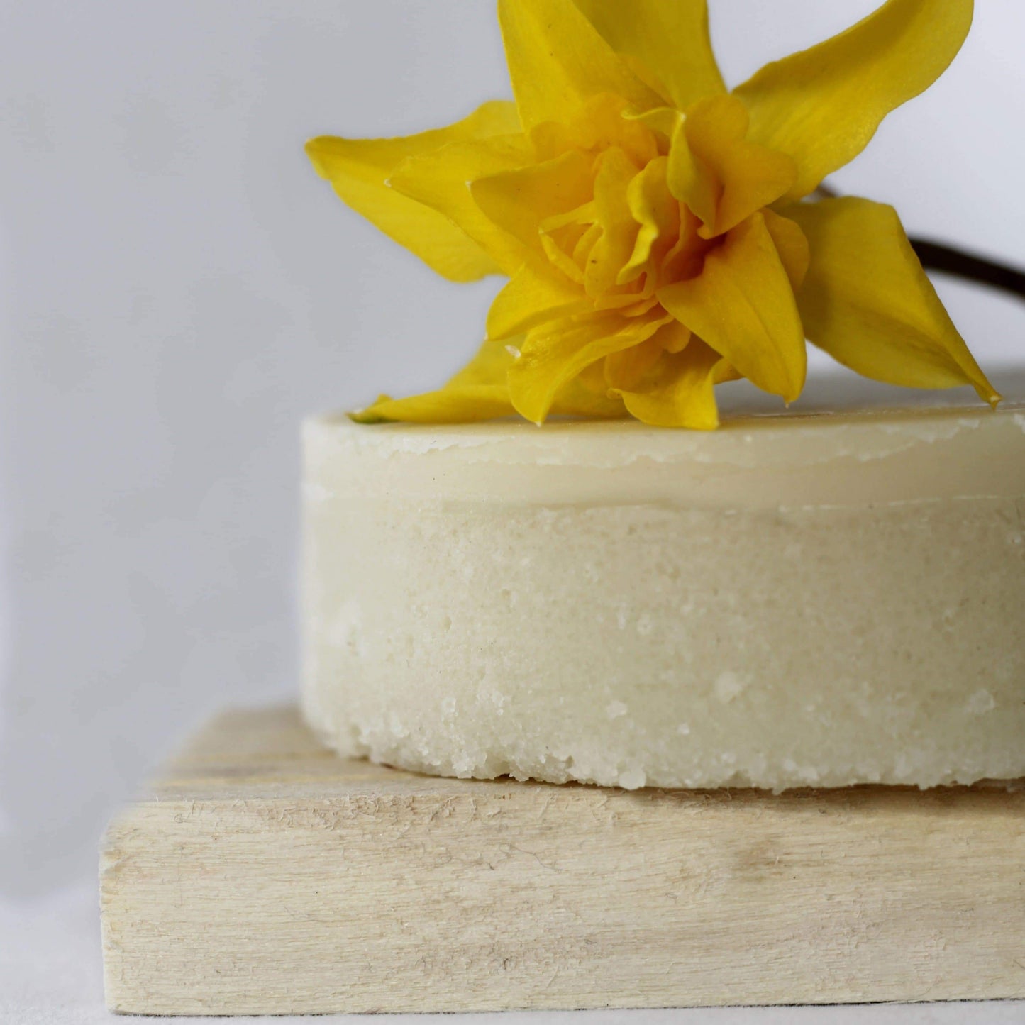 Pale yellow lotion bar on a wooden soap holder with a bright yellow flower sitting on top.