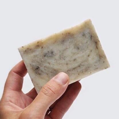 Cream soap bar with gray swirls being held in hand on a white background.