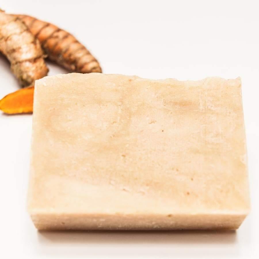 Pale orange soap bar on a white background with turmeric behind the soap.